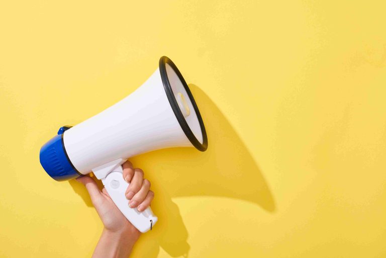 Cropped view of a woman holding a yellow loudspeaker.